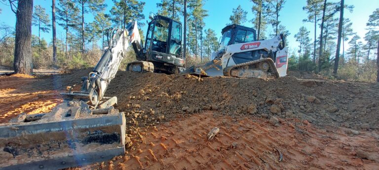 Two construction machines parked on a dirt road, surrounded by a construction site and scattered debris.
