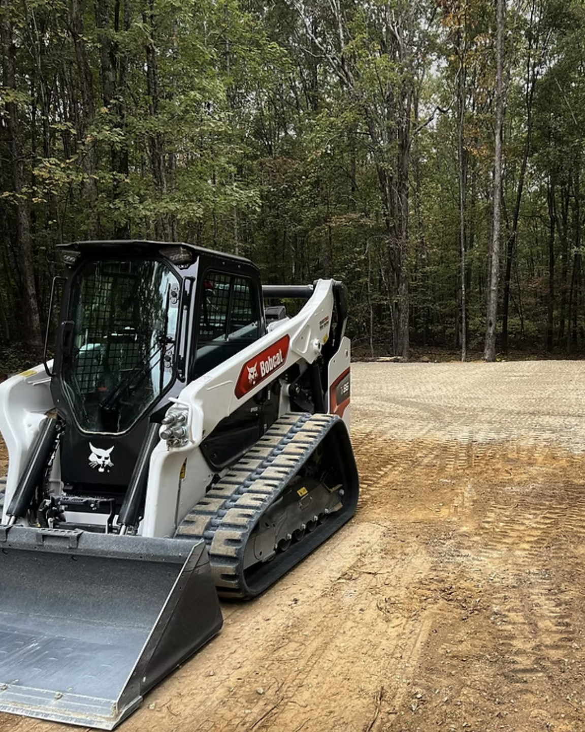 A small skid steer loader parked on a dirt road, surrounded by natural scenery and clear blue skies.