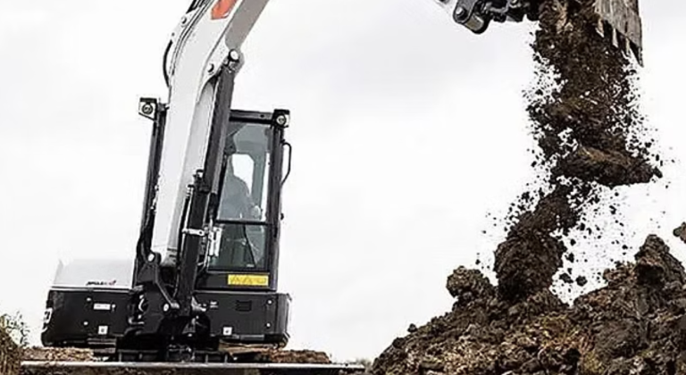 A small excavator digging dirt in a field, with soil being displaced and a clear blue sky in the background.
