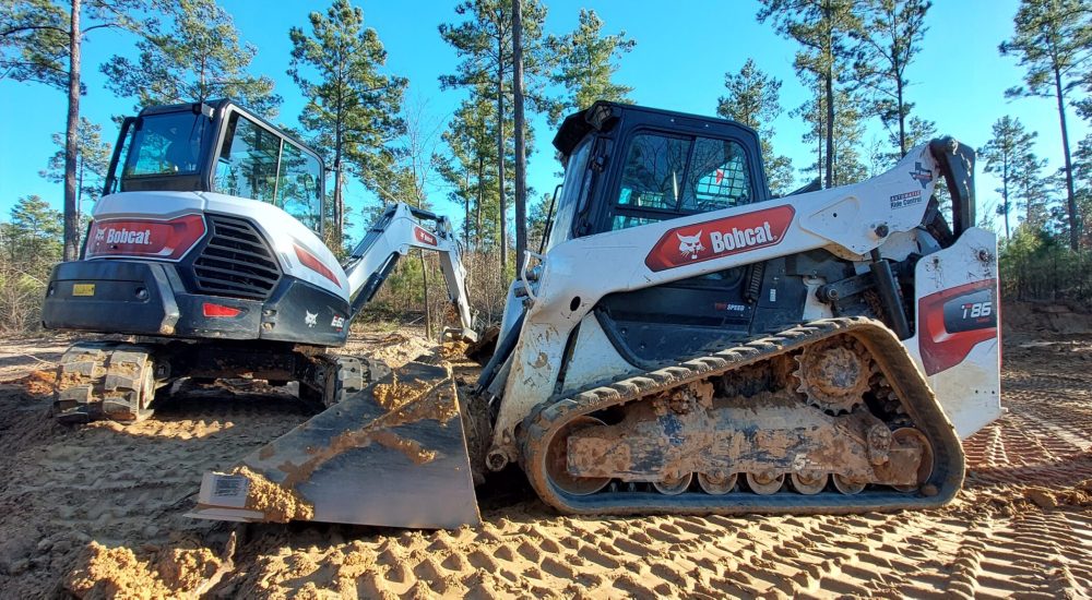 Two small construction machines parked on a dirt road, surrounded by earth and gravel.